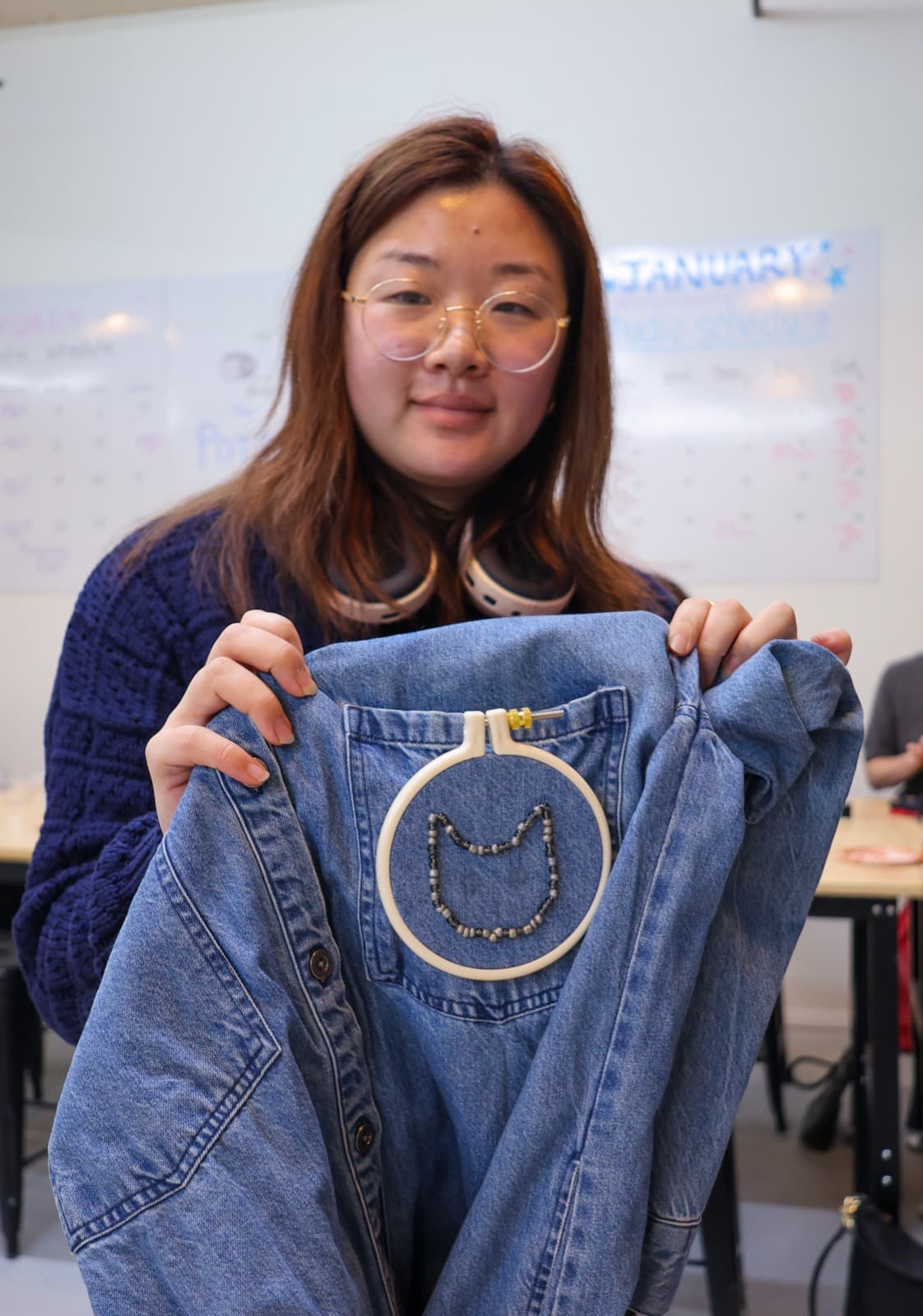 Student holding up denim jacket with beaded cat-face embroidery