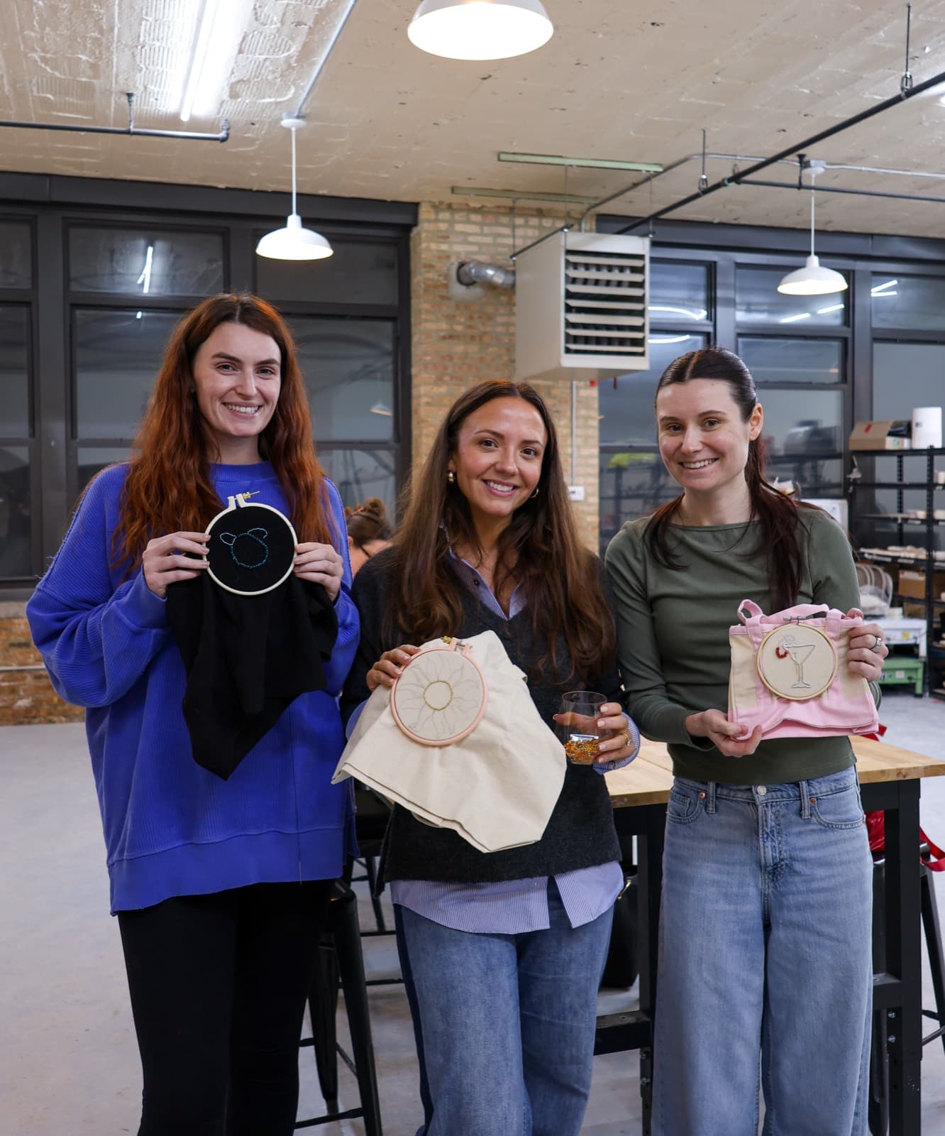 Three students holding their finished beaded embroidery pieces in hoops